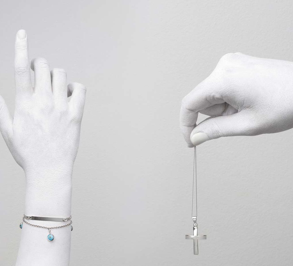 two hands one with a silver cross and the other with bracelet